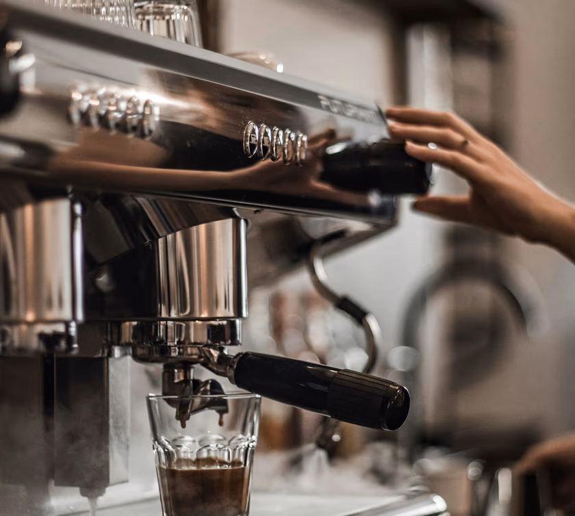 A hand on the group head of an espresso machine as a shot pours into a glass
